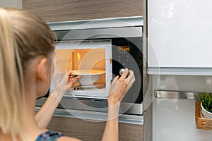 Woman warm up the food in microwave oven at home photo