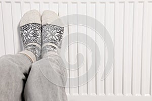 Woman warming feet near heating radiator, closeup