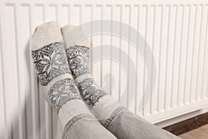 Woman warming feet near heating radiator, closeup