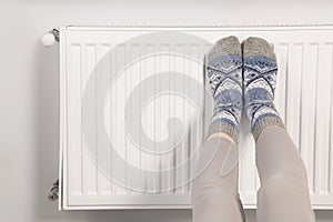 Woman warming feet near heating radiator, closeup. Space for text