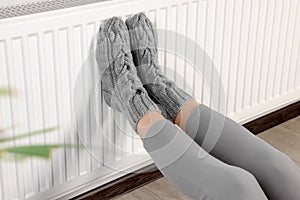 Woman warming feet near heating radiator indoors, closeup