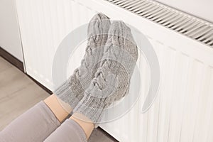 Woman warming feet near heating radiator indoors, closeup