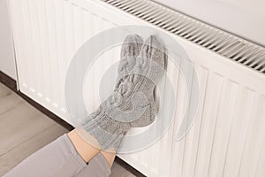 Woman warming feet near heating radiator indoors, closeup