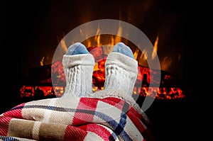 Woman warming feet in woolen socks near fireplace