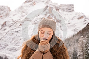 Woman warming hands with breathe among snow-capped mountains