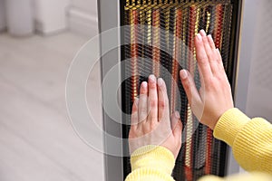 Woman warming hands near heater indoors, closeup