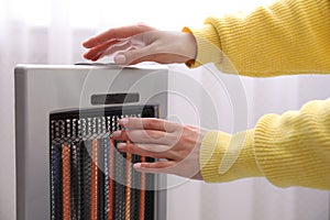 Woman warming hands near heater indoors, closeup