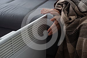 Woman warming hands near heater indoors, closeup