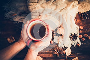 Hands in red knitted gloves holding a hot cup of coffee against yellow leaves background. Concept of autumn time, warmth and cozin