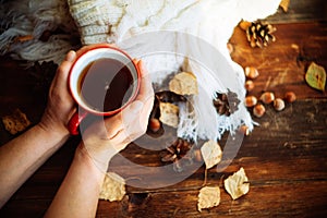 Hands in red knitted gloves holding a hot cup of coffee against yellow leaves background. Concept of autumn time, warmth and cozin