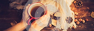 Hands in red knitted gloves holding a hot cup of coffee against yellow leaves background. Concept of autumn time, warmth and cozin