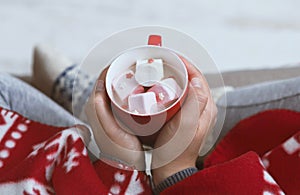 Woman warming with hot chocolate at home bundling in red plaid