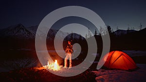 Woman warming up in a camping by the fire in mountains