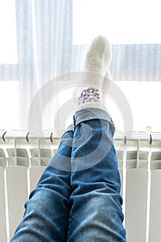 Woman warming up with feet on heater wearing woolen socks