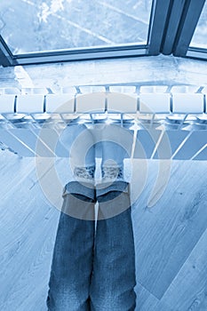 Woman warming up with feet on heater wearing woolen socks, view from above