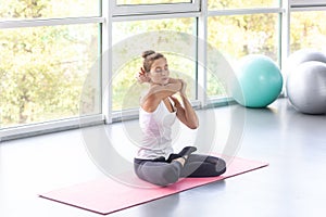 Woman warming up her hands, training and stretching arm before workout, sitting on yoga mat.