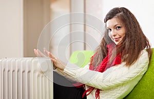 Woman warms hands near calorifer at home