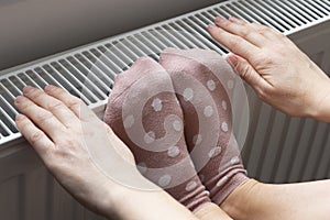 A woman warms her feet and hands on a radiator