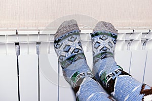 A woman warms her frozen feet in socks on a battery. The concept of heat in the house. Cold season.