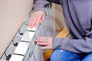 A woman warms her frozen hands on the battery. The concept of heat in the house. Cold season.