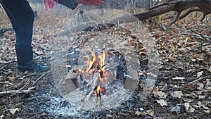 A woman warms her hand over a fire in cold autumn forest