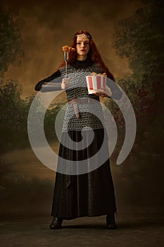 Woman warrior in chainmail and dress posing junk food and fork with chicken as her sword against vintage studio