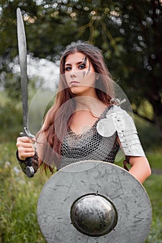 A woman warrior with combat makeup in a chainmail top with plate shoulder pads and bracers poses in a combat