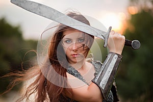 A woman warrior with combat makeup in a chainmail top with plate shoulder pads and bracers poses in a combat