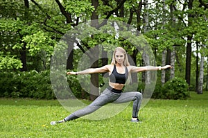 Woman in warrior pose in Park among greenery, slender blonde girl doing yoga