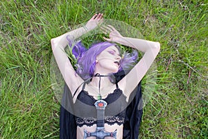 Woman warrior with violet hair in a long black cloak in the field, cosplay
