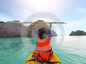 The woman was raising his hand holding a paddle on a kayak that was floating surrounded