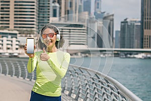 Woman was running along Dubai Marina embankment and listens to music with headphones and shows the white screen of her