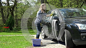 woman wash black car window with foamy sponge in garden. 4K