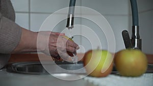 woman washes an apple in the kitchen under the tap close-up