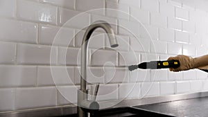 A woman washes ceramic tiles in a bathroom with a steam generator. Steam cleaning tiles with Karcher. Cleaning kitchen