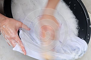 A woman washes clothes by hand in the soapy water, isolated on white background.