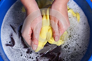 A woman washes clothes with her hands in soapy water. Hand wash clothes.