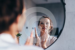 Woman washes in front of the mirror, applying foam to her face photo