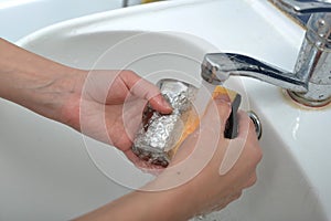 A woman washes an iron glass in a white sink under a stream of water