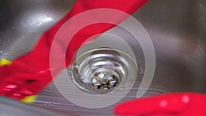 Woman washes a metal faucet with sponge in the kitchen in red gloves. Hands close-up.