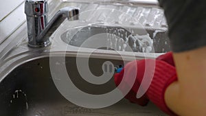 Woman washes a metal sink in the kitchen in red gloves. Hands close-up.