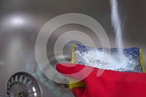 Woman washes a metal sink with sponge in the kitchen in red gloves. Hands close-up.