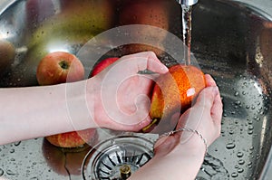 Woman washes an pear under running water. Metal sink in the kitchen. Hands with pear closeup