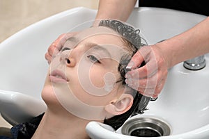 A woman washes a young man`s head in a beauty salon. Female hands of the hairdresser soap the hair of the guy before the haircut.