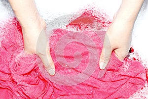 Woman washing clothes by hand with detergent in plastic bowl