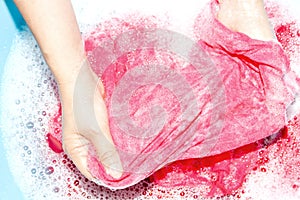 Woman washing clothes by hand with detergent in plastic bowl