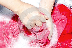 Woman washing clothes by hand with detergent in plastic bowl