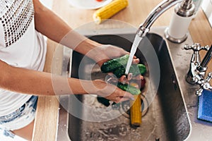 Woman washing cucumbers in kitchen sink close up.
