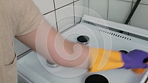 Woman washing dirty gas stove with a sponge.