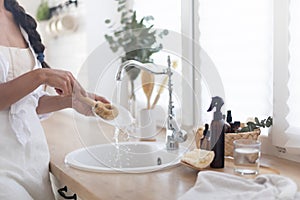 Woman washing dishes with detergent on kitchen. Eco brush with foam and basket on white bright kitchen.